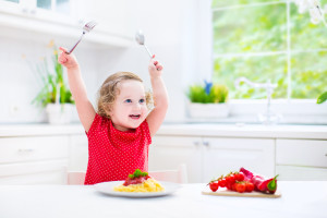 Funny toddler girl eating spaghetti in white kitchen